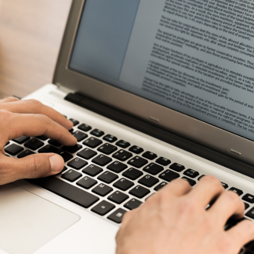 Mãos digitando em um laptop, com tela mostrando um documento de texto, em ambiente de trabalho para escrita e histórias para escrever