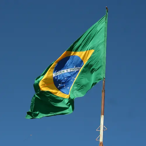 Bandeira do Brasil hasteada, tremulando ao vento contra um céu azul, representando a literatura brasileira e a escritoras brasileiras.